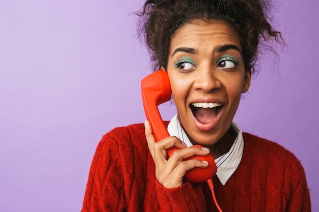 Portrait of cute african american woman with afro hairstyle screaming while holding red handset, isolated