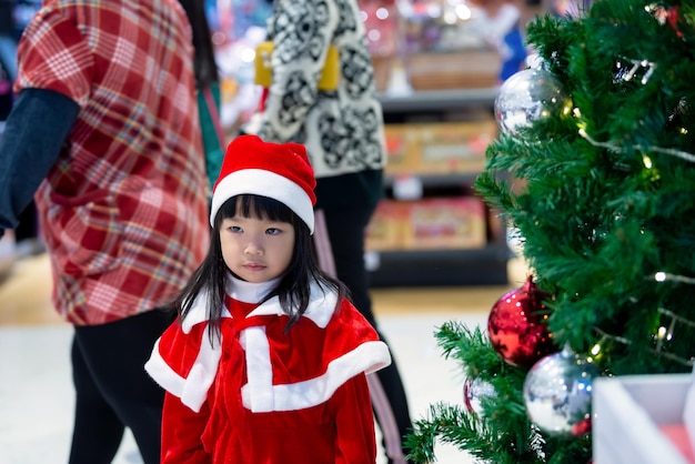 Portrait of cute asian little girl wear santa dress happy near christmas treeThailand kid join christmas festival