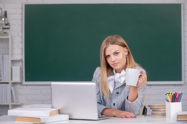 Portrait of cute attractive young woman student drinking coffee or tea in university or high school ...