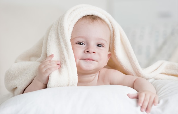 Portrait of cute baby boy lying under white blanket on bed