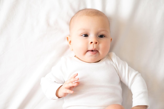 Portrait of a cute baby girl of 5 months in a white bodysuit on a white bed Space for text lifestyle