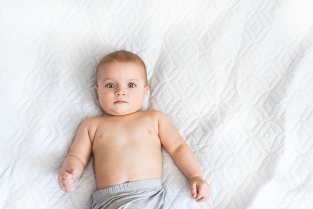 Portrait of a cute baby of nine months. small boy watches with interest what is happening on the bed