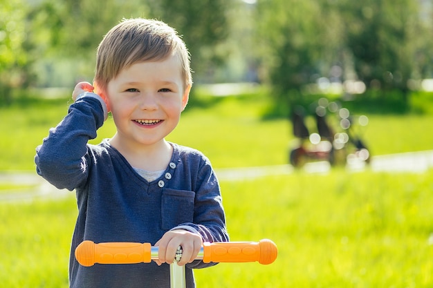 Portrait of cute baby (son) on a scooter in the park on a background of green grass and trees