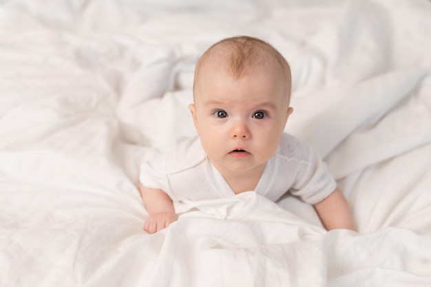 portrait of a cute baby in a white bodysuit on a bed at home with white linens. Newborn baby at home