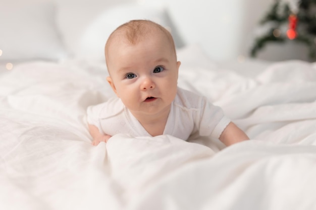 portrait of a cute baby in a white bodysuit on a bed at home with white linens. Newborn baby at home