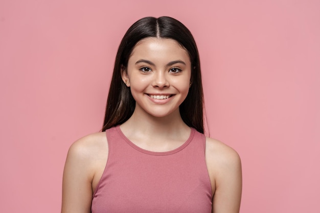 Portrait of cute beautiful teenage girl in pink top looking at camera isolated on pink background