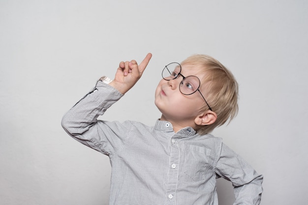 Portrait of a cute blond boy with big glasses. Finger pointing up. 