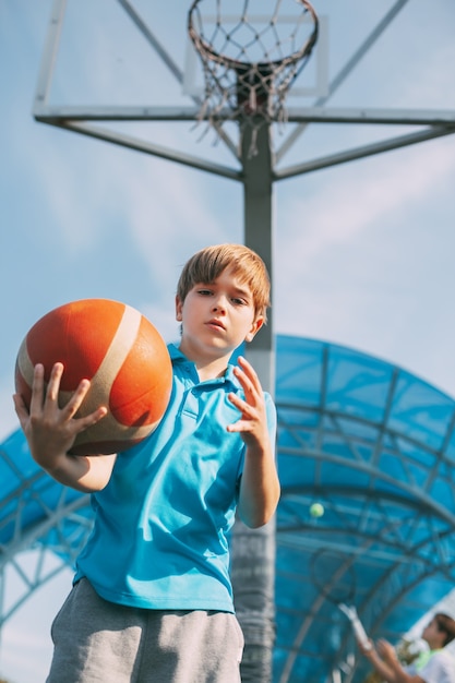 Portrait of a cute boy basketball player standing with a ball in his hands next to the basketball