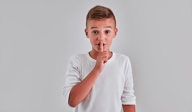 Portrait of a cute boy on a gray background, which put a finger to his lips shows quietly, a secret.