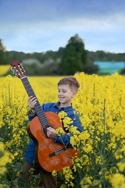 Portrait of cute boy playing a guitar in the summer yellow field. Child having fun imagining himself as a superstar.