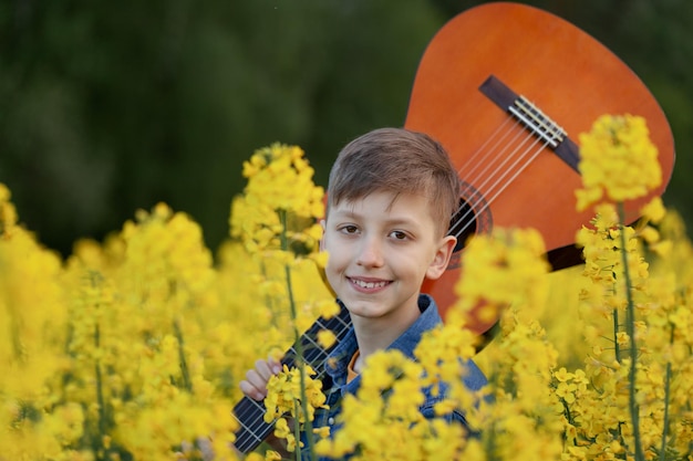 Portrait of cute boy playing a guitar in the summer yellow field. Closeup portait smiling child