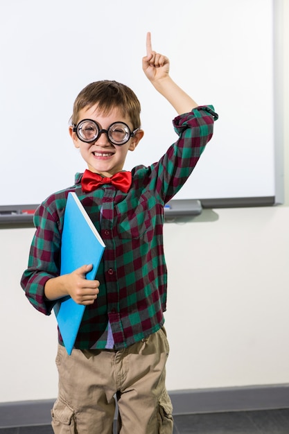 Portrait of cute boy with notebook raising hand in classroom