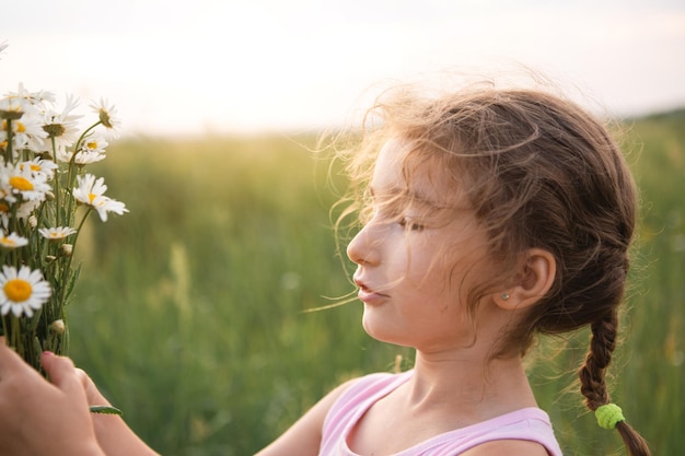 Portrait cute child girl with a bouquet of chamomile in summer on a green natural background Happy child hidden face no face covered with flowers Copy space Authenticity rural life ecofriendly