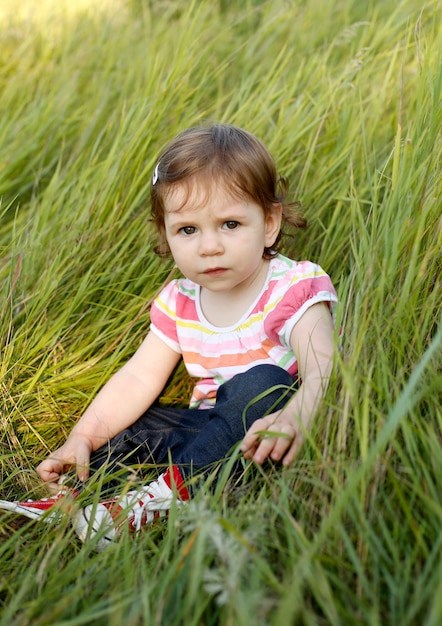 Portrait of cute curly toddler girl sit in long grass