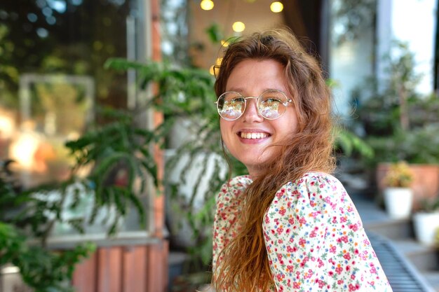 Portrait of a cute girl in glasses in a cozy green cafe smiles rests relaxes and looks at the camera