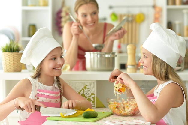 Portrait of cute girls with mother preparing delicious fresh salad in kitchen