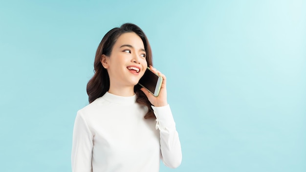 Portrait of a cute happy girl in dress talking on mobile phone and laughing isolated over blue background