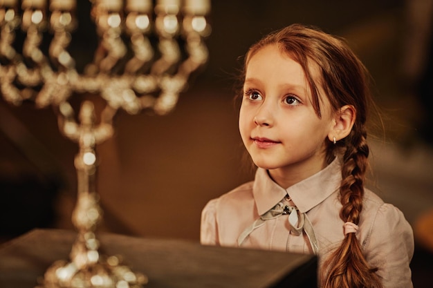 Portrait of cute jewish girl looking at menorah candle during hanukkah celebrations