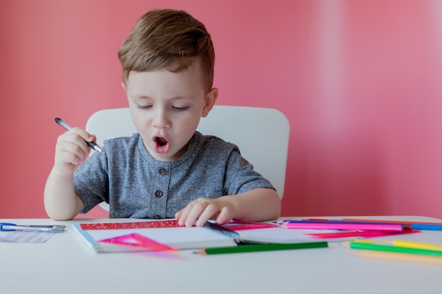 Portrait of cute kid boy at home making homework Little concentrated child writing with colorful pencil indoors Elementary school and education Kid learning writing letters and numbers