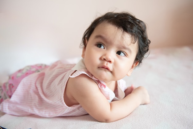 Portrait of a cute little Asian baby girl wear pink dress lying on bed, looking out