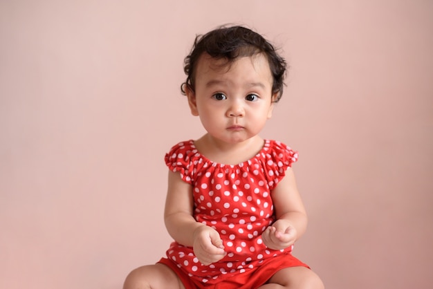 portrait of a cute little asian baby girl wear red dress on a beige background