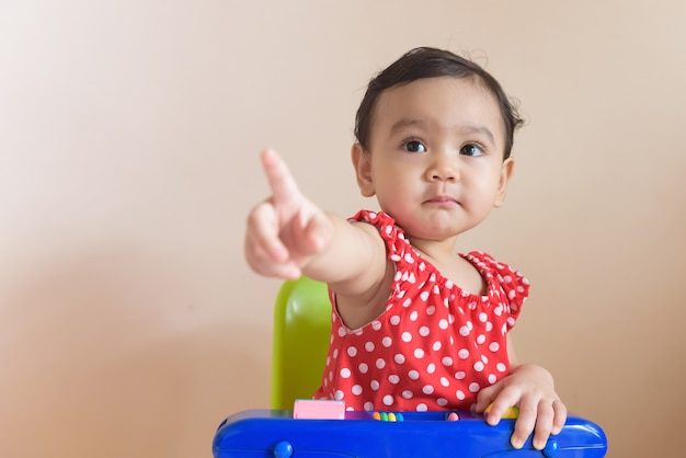 Portrait of a cute little Asian girl dressed in red sitting with her finger pointing forward, isolated on the background baby expression concept