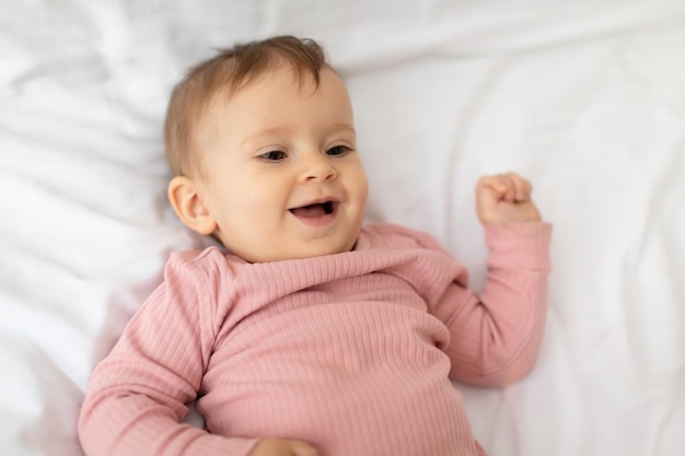 Portrait of cute little baby girl lying and smiling posing on white blanket on bed above view shot