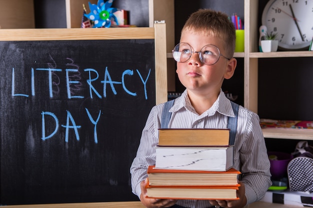 Portrait of cute little boy holding book in classroom. Happy International Literacy Day.