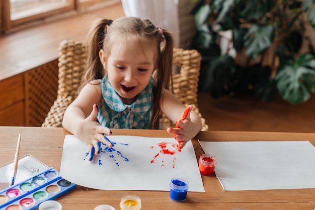 Portrait of a cute little girl draws with paints and hands Painted childrens palms