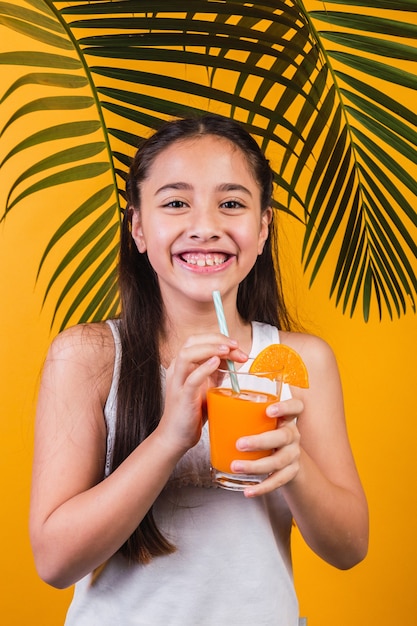 Portrait of a cute little girl enjoying orange juice on a yellow background.