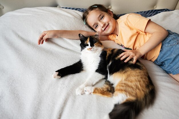 Portrait of a cute little girl lying on the bed with her cat