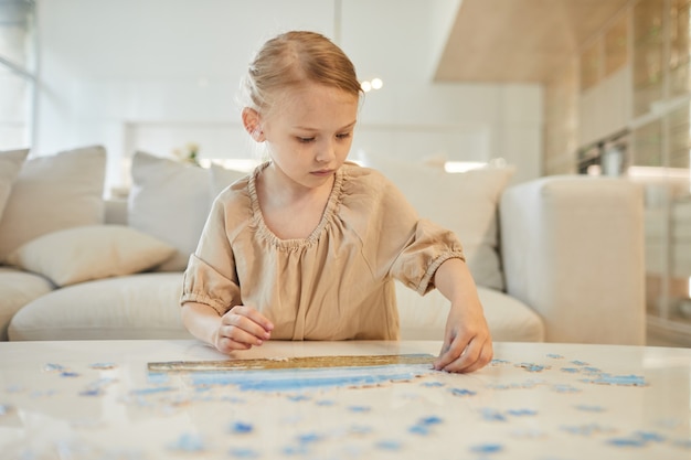 portrait of cute little girl solving jigsaw puzzle while enjoying time indoors at home