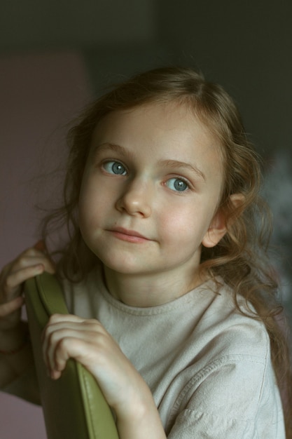 Portrait of a cute little girl with curly hair sitting on a green chair in a room in a light dress