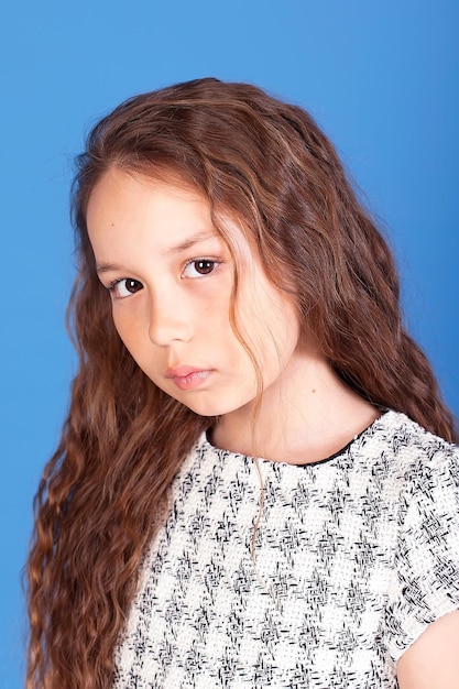 Portrait of a cute little girl with a stylish curly hairstyle standing and looking at the camera with a cheerful attentive face calm expression A closed studio shot isolated on a gray background