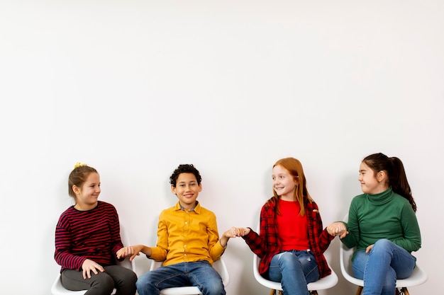 Portrait of cute little kids in jeans  sitting in chairs on white wall