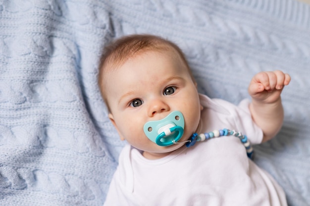 Portrait of cute newborn baby with a pacifier in his mouth lying on his back on blue knitted blanket. breastfeeding. concept of a happy childhood and motherhood. a healthy child. High quality photo