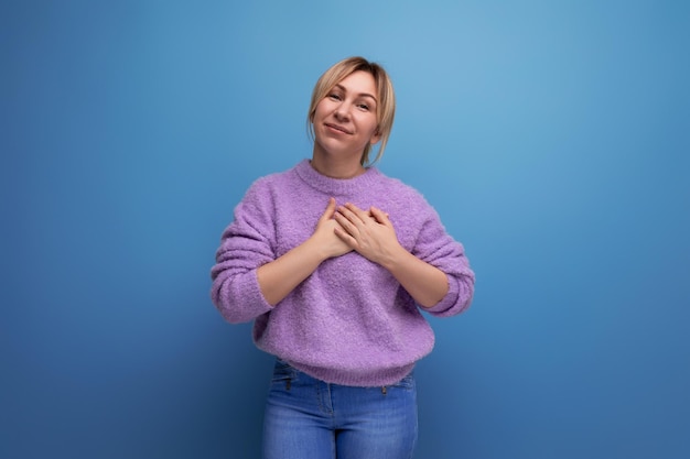 Portrait of a cute pleasant blond young woman smiling with love on a bright plain background