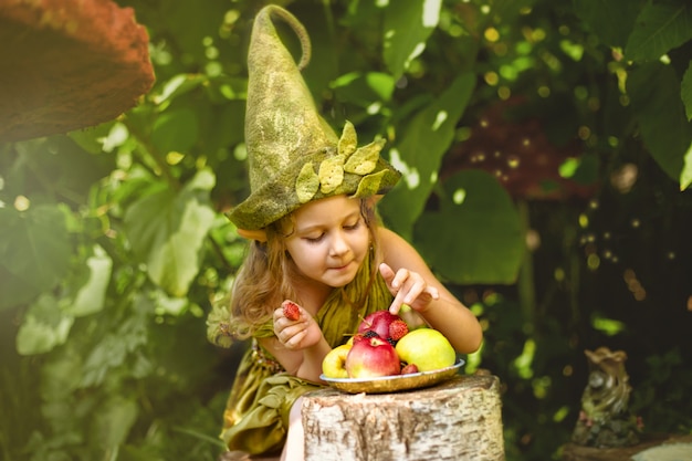 Photo portrait of a cute pretty girl in a gnome eats berries and apples on a plate.