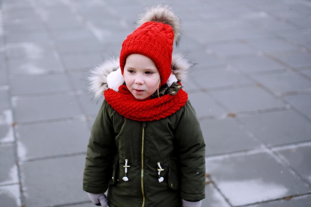 Portrait of cute sad little girl in warm outerwear clothing standing outdoors alone in cool weather