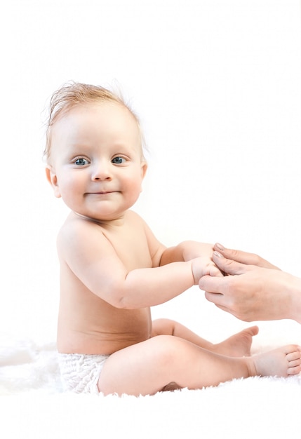 Portrait of a cute six month old baby sitting on the bed holding mom's hands. mother holding her cute baby son