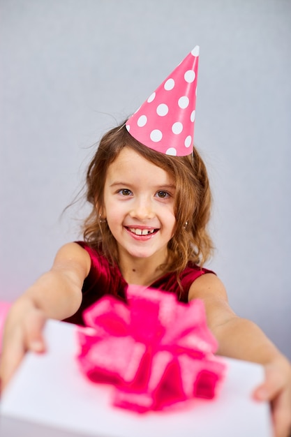 Portrait cute smiling girl in birthday hat holding a pink and white gift box