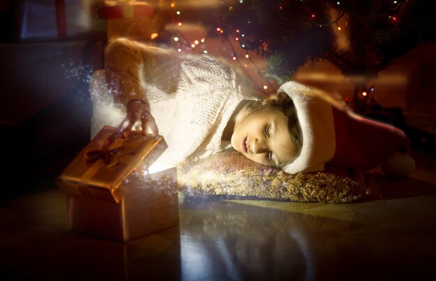 Portrait of cute smiling girl lying on floor and looking inside of magic glowing box