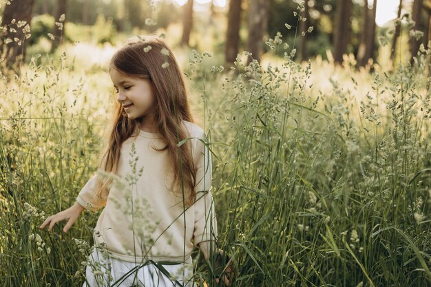 Photo portrait of a cute smiling girl with beautiful hair posing for a photo in the middle of tall grass in a coniferous forest at sunset