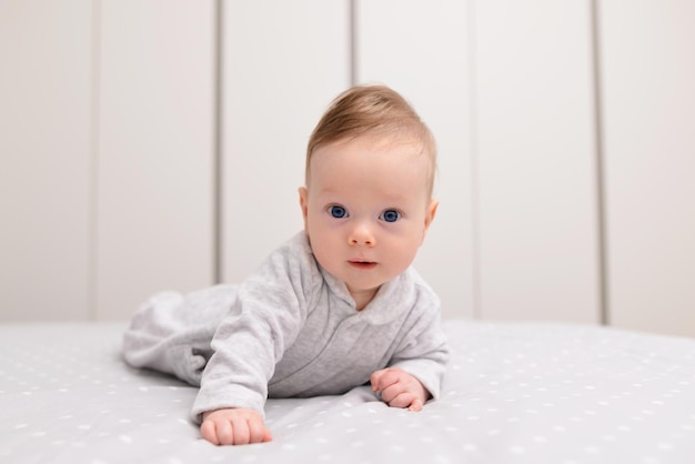 Portrait of cute smiling happy baby boy crawling on bed on the white blanket in bedroom