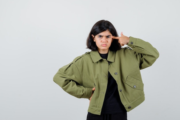 Portrait of cute teen girl showing suicide gesture in army green jacket and looking depressed front view