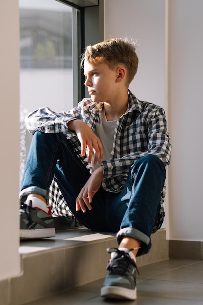 Portrait of a cute teenager in casual clothes A young guy sits on the floor in a building and looks out the window