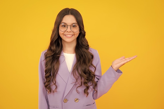 Portrait of cute teenager child girl pointing hand showing adverts with copy space over yellow background