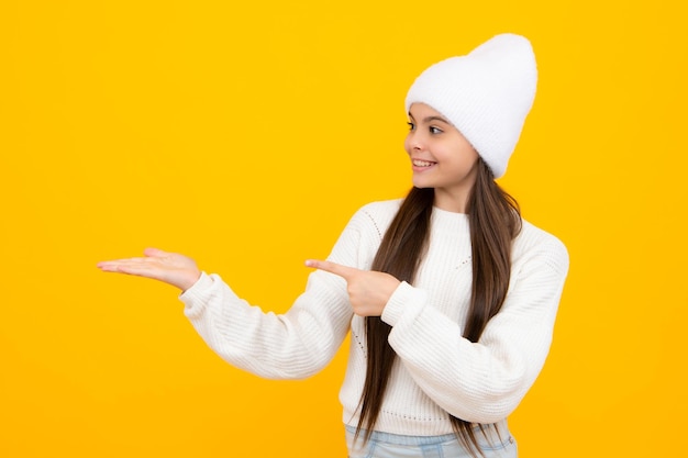 Portrait of cute teenager child girl pointing hand showing adverts with copy space over yellow 