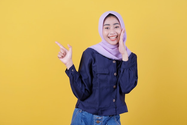 Portrait of cute woman pointing up in casual cloth wearing hijab on isolated yellow background