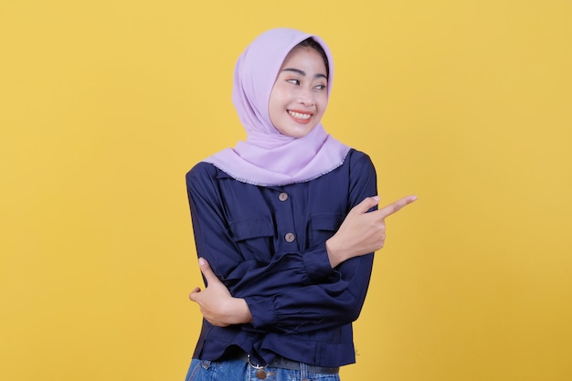 Portrait of cute woman pointing up in casual cloth wearing hijab on isolated yellow background